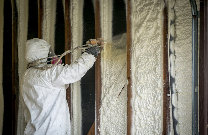 A worker applying closed-cell spray foam insulation onto a surface.